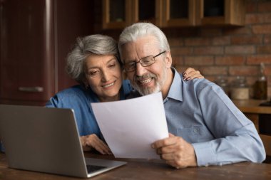 Gülümseyen olgun çift iyi haberlerle mektup okuyor, dizüstü bilgisayar kullanıyor.