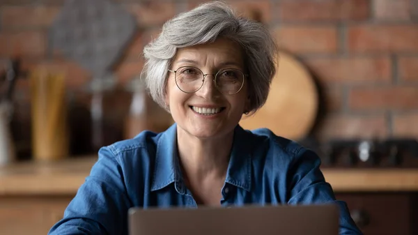 Портрет с улыбкой на голове взрослой женщины в очках с помощью ноутбука — стоковое фото