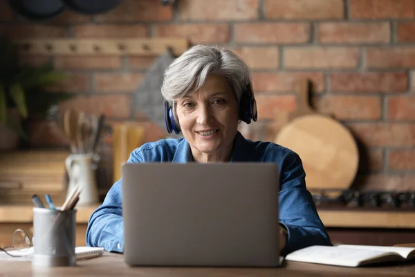 Leende mogen kvinna bär hörlurar med bärbar dator hemma — Stockfoto