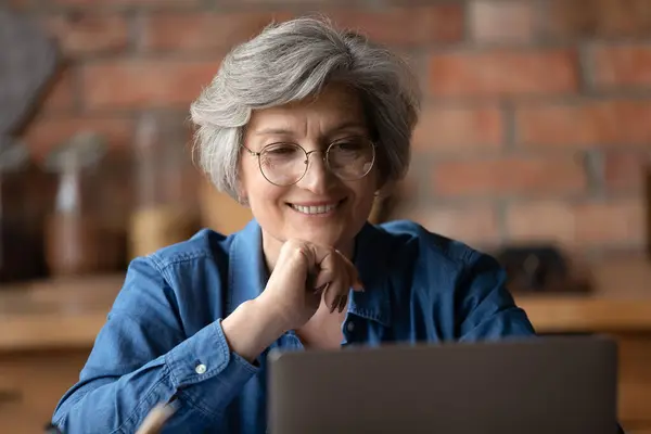 Zblízka usměvavá zralá žena nosí brýle při pohledu na obrazovku notebooku — Stock fotografie