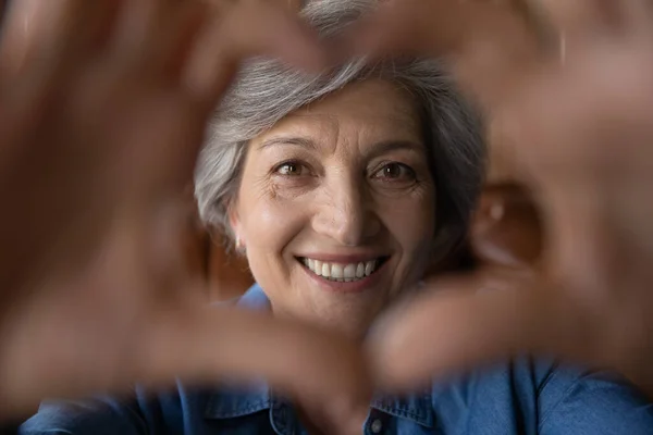 Close up sorridente donna dai capelli grigi maturo mostrando gesto del cuore — Foto Stock