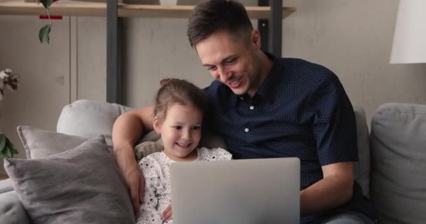 Father and daughter relaxing on couch with laptop watching cartoons — Stock Video