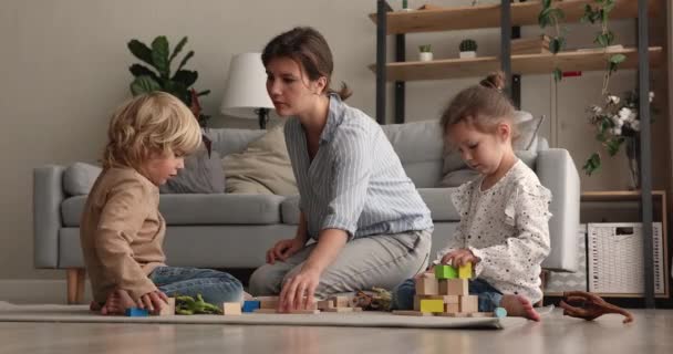 Молодая мать и младшие братья и сестры играют в деревянные блоки дома — стоковое видео