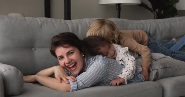 Młoda mamusia jej małe dzieci bawią się razem leżąc na kanapie — Wideo stockowe
