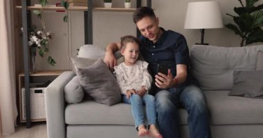 Baba ve kızı akıllı telefon kullanarak kanepede dinleniyorlar.