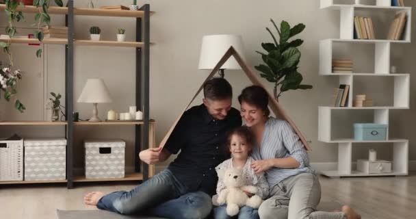 Happy homeowners sit under carton roof smile look at camera — Stock Video