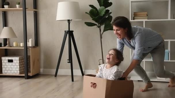 Madre montando hija mientras ella se sienta dentro de la caja de cartón — Vídeos de Stock