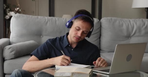 Guy memakai headphone mendengarkan kursus audio pada catatan menulis laptop — Stok Video