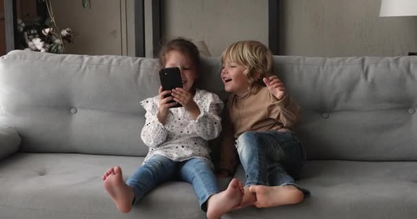 Les enfants s'assoient sur le canapé en s'amusant avec un téléphone intelligent — Video