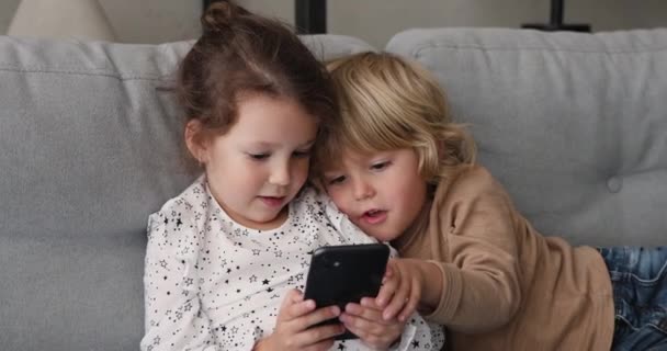 Kislány és fiú pihen a kanapén okostelefonnal — Stock videók