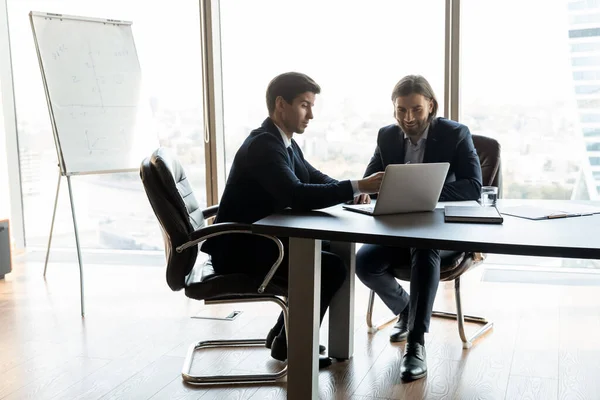 Smiling business partners work on laptop in office