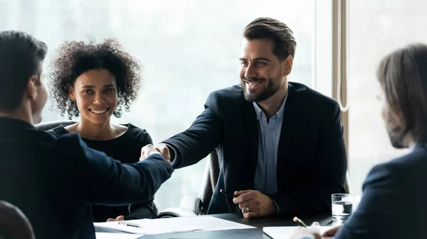 Усміхнені бізнесмени потискають руки, закриваючи угоду на зустрічі — стокове фото