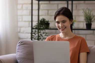 Gülümseyen genç bir kadın evde bilgisayar kullanıyor..