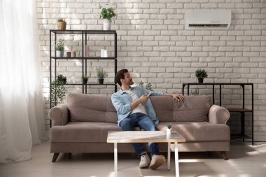 Rahatlamış genç adam evdeki klima sistemini çalıştırıyor..