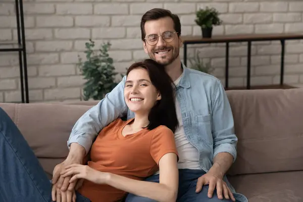 Retrato de una joven y sonriente pareja familiar relajándose en el sofá. —  Fotos de Stock
