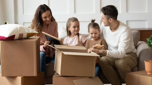 Família mudou-se para casa nova sentado no sofá desempacotando pertences — Fotografia de Stock