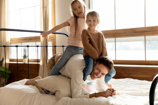 V ložnici si s tátou hrají dvě veselé dcerky. — Stock fotografie