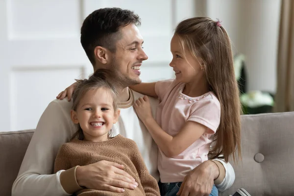 Père assis sur le canapé embrassant deux petites filles — Photo