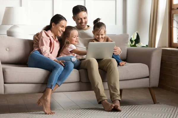 Famille avec des filles se détendre sur le canapé en utilisant un ordinateur portable regarder des dessins animés — Photo