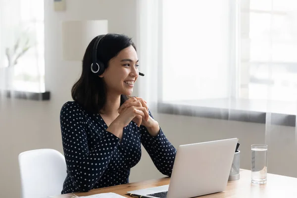 Glimlachende aziatische zakenvrouw dragen headset met behulp van laptop, op zoek naar opzij — Stockfoto