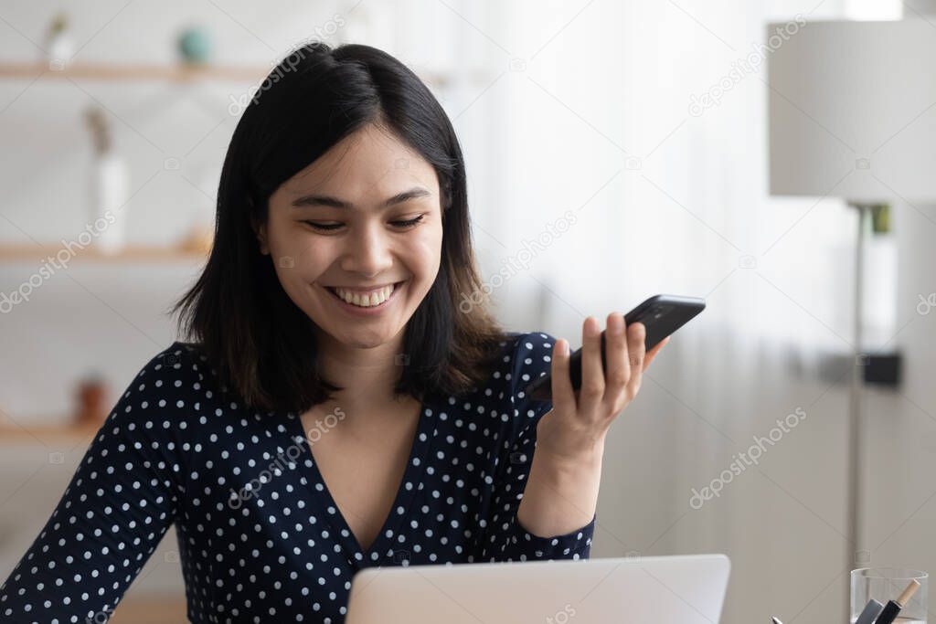 Close up smiling Asian woman holding phone, listening voice message