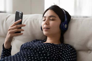 Kapat telefonu kullanarak kulaklık takan mutlu Asyalı genç kadın.