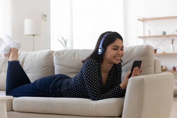 Smiling relaxed Asian young woman wearing headphones using phone — Stock Photo, Image