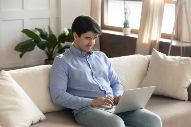 Sakin genç erkek, dizüstü bilgisayarla kanepede dinleniyor.