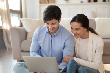 Mutlu milenyum çifti yerde oturup dizüstü bilgisayar ekranında dinleniyor.