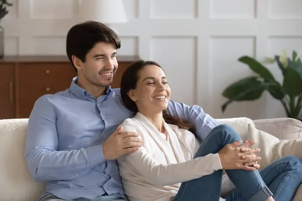 Lächelndes Millennial-Paar umarmt sich auf gemütlicher Couch und schaut träumend zur Seite — Stockfoto