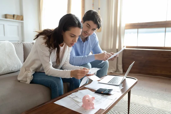 Geconcentreerd duizendjarig paar dat op de bank zit en betrokken is bij het lezen van documenten — Stockfoto