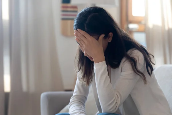 Депресивна молода жінка плаче на дивані, покриваючи обличчя долонею — стокове фото