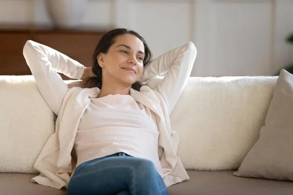 Wanita yang sukses beristirahat di sofa sambil melihat ke samping dengan senyum yang menawan — Stok Foto