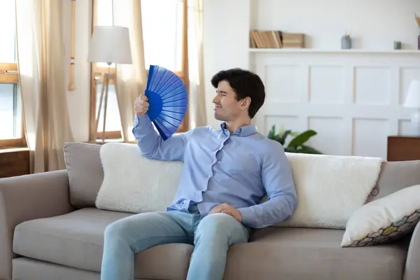 Young man houseowner saving himself from heat using paper weaver — Stock Image Young man houseowner saving himself from heat using paper weaver Stock Image