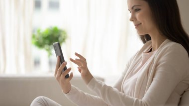 Kanepede oturmuş akıllı telefon kullanan genç bir kadın.