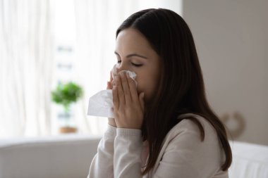 Kapalı gözlerle oturan hasta kadın, burnunu mendile gizliyor.