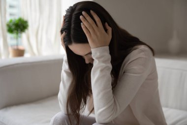 Stresli, kafası karışmış genç bir kadın, koltukta oturuyor ve sarılıyor.