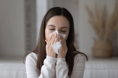 Hapşıran zayıf genç kadın kağıt peçeteye burnunu siliyor.
