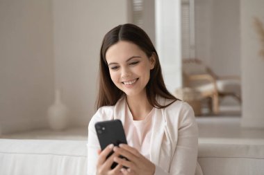 Kanepede oturan pozitif genç bayan akıllı telefondan sohbetin tadını çıkarıyor.