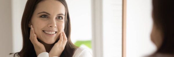 Зеркальное отражение счастливой женщины тысячелетия, наслаждающейся шелковистой кожей лица