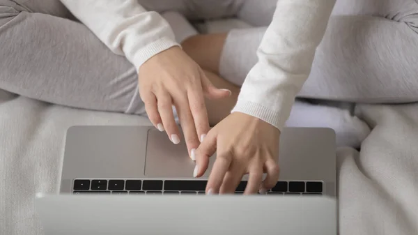 Ocupada joven freelancer sentada con las piernas cruzadas en el sofá usando el ordenador portátil — Foto de Stock