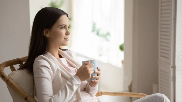 Tranquil woman sitting in armchair by window drinking tea relaxing — Stock Photo, Image