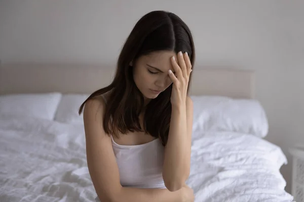 Frusztrált fiatal nő ül az ágyon szenved hirtelen fejfájás — Stock Fotó