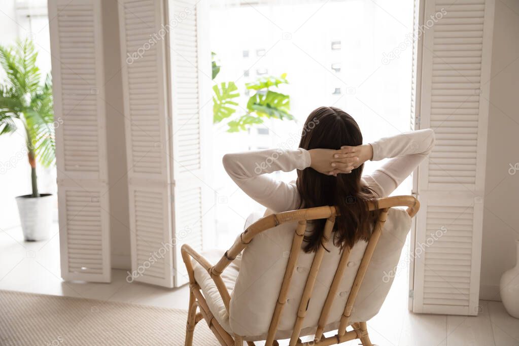 Successful millennial female relaxing in armchair enjoying scene from window