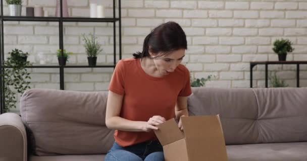 Счастливая миллениалка открывает картонную посылку дома. — стоковое видео