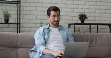 Rahatlamış gülümseyen genç yakışıklı adam evde bilgisayar kullanıyor..