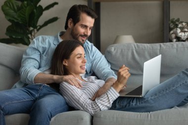 Kafkasyalı çift kanepede dizüstü bilgisayar kullanarak rahatlıyor.