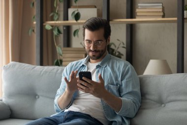 Genç beyaz adam kanepeye uzanıp akıllı telefon kullanıyor.