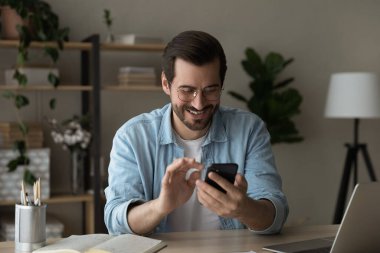 Mutlu genç adam interneti cep telefonuyla tarıyor.