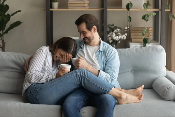 Overjoyed young couple relax on couch drinking coffee — Stock Photo, Image